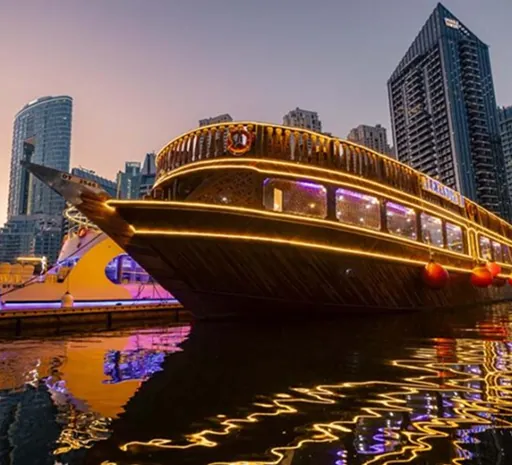 Wooden dhow boat lit up at night among skyscrapers